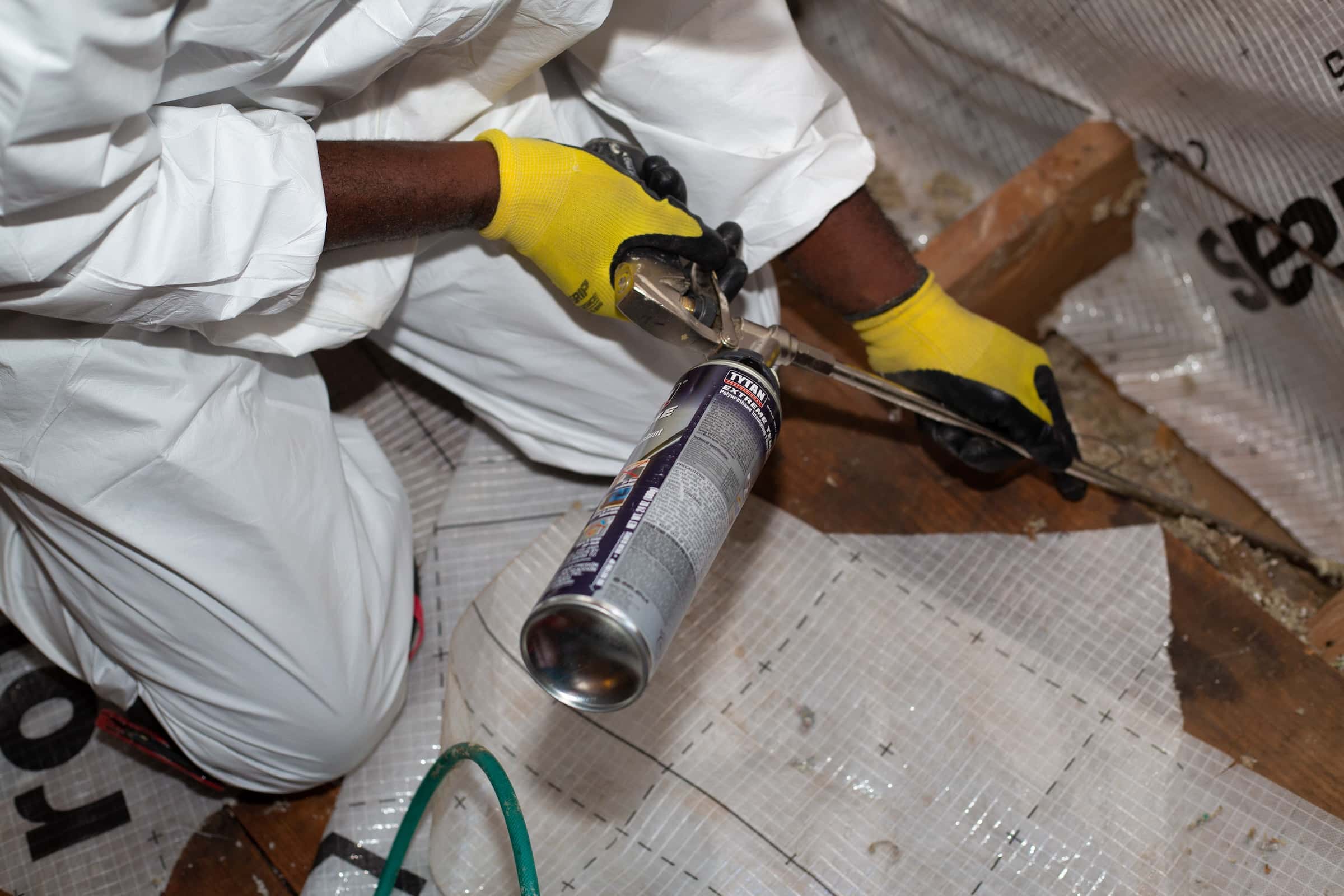 Hands using an air sealing gun to apply caulk to gaps in attic